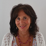 Portrait of a smiling woman with shoulder-length dark hair, wearing a white lace top and pink bead necklace.